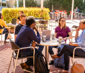 Students sitting around a cafe table with coffees chatting and smiling.