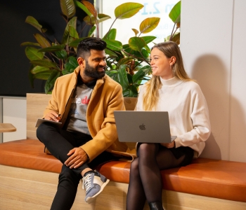 Two students sit together chatting with a laptop