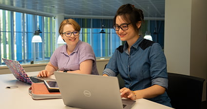 Two students sitting at a desk with laptops