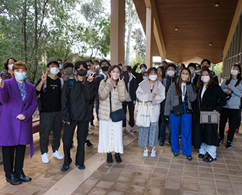 Group of international students wearing masks stand next to Professor Cobie Rudd. They are standing in front of a building on ECU's South West campus