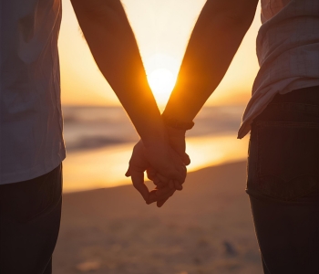 Two people holding hands walking towards a sunset.