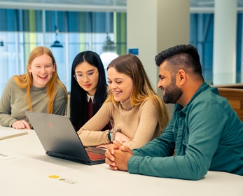 Four students all looking at a shared computer in the library