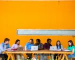 Three students sitting around an orange desk inside a university library studying together. 